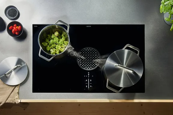 Aufnahme von oben: Schwarzes BORA Induktionskochfeld mit integriertem Dunstabzug. Dampf aus einem Topf mit Romanesco wird effizient abgesaugt.